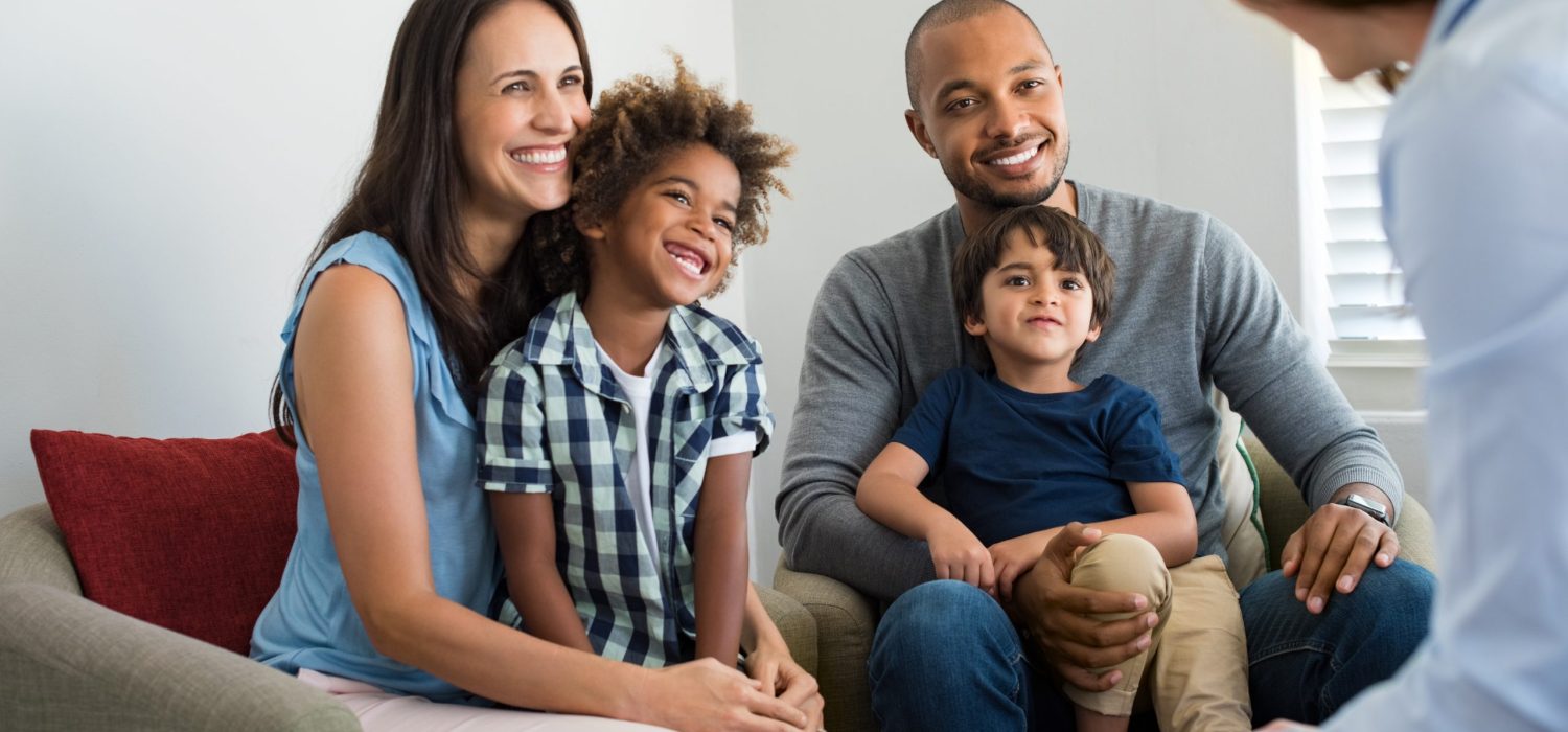 Family talking with counselor Happy young family sitting on couch and talking with family counselor. Smiling parents with adopted children discussing with counselor. Multiethnic family meeting a financial agent.